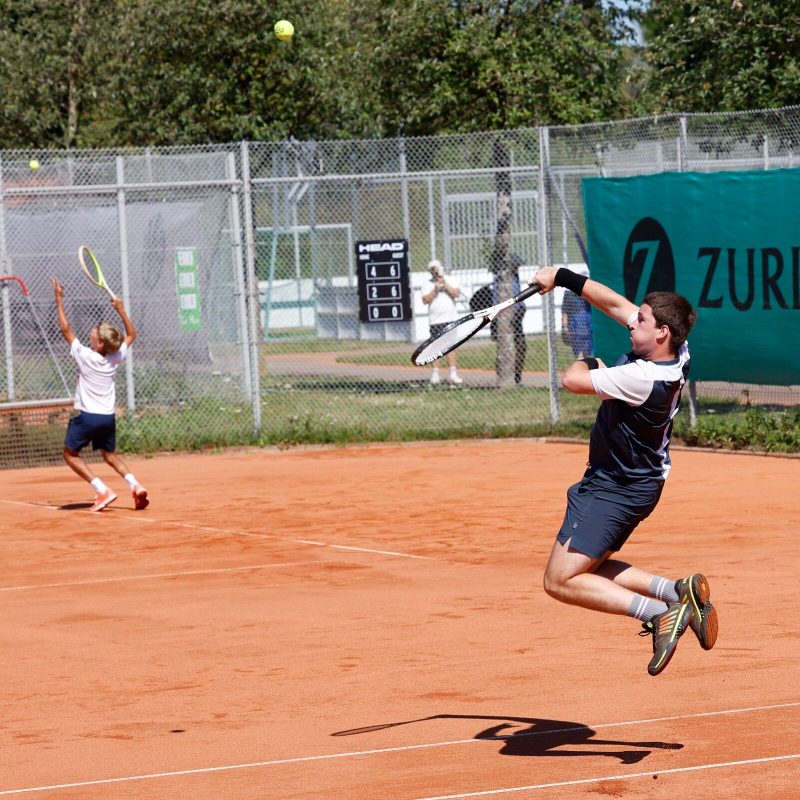 Junger Spieler springt beim Aufschlag vom Sand ab